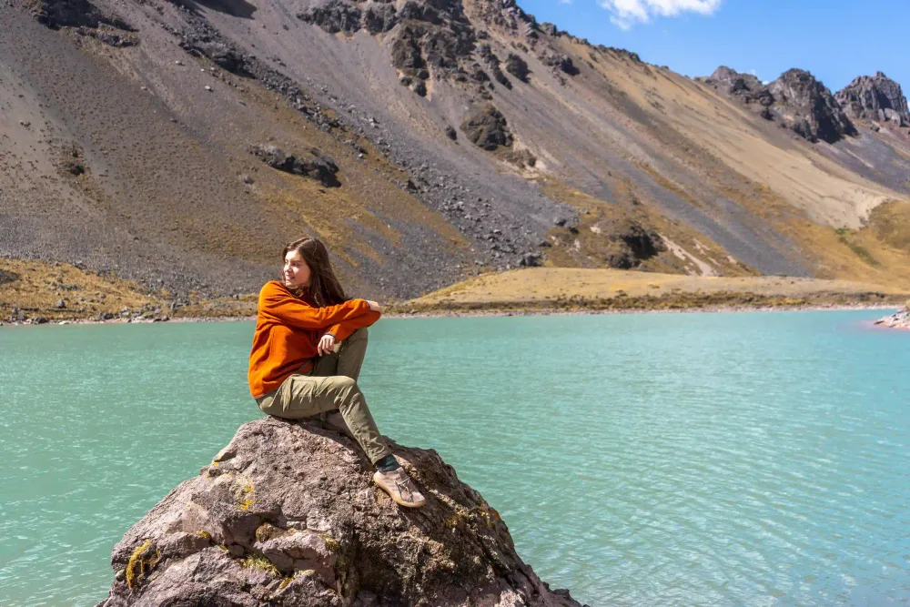 A traveler resting on a rock beside a turquoise Ausangate lake