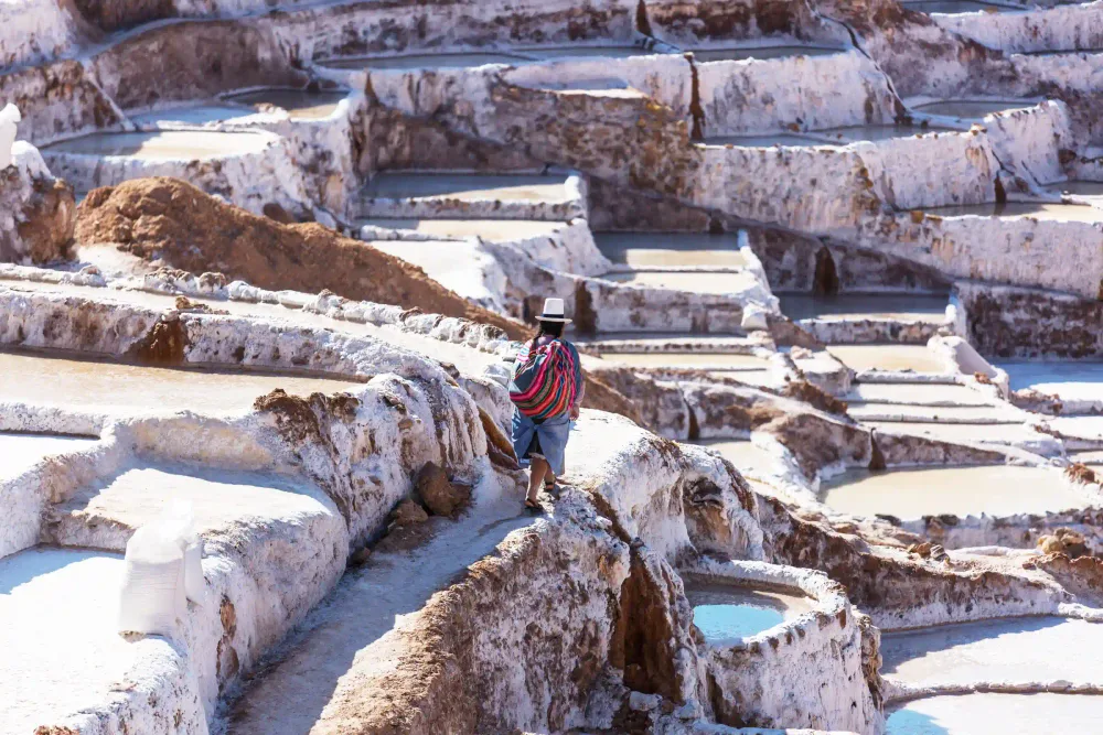 A visitor walking along the paths between the Maras salt pools