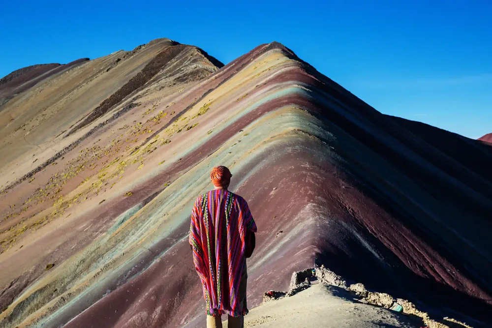A traveler in a red poncho looking out over Rainbow Mountain near Cusco